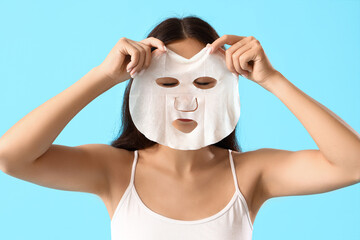 Young woman with sheet facial mask on blue background