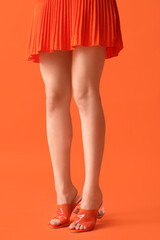 Legs of young woman in stylish orange sandals on color background