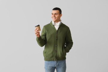 Fototapeta premium Young man in knitted sweater with cup of coffee on light background