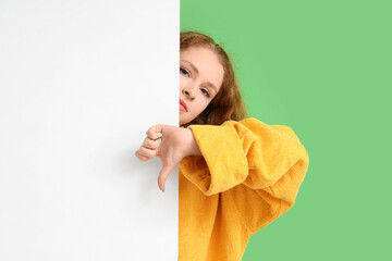 Young woman with blank poster showing dislike on green background