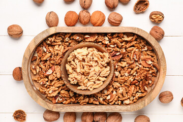 Bowl with tasty walnuts on white wooden background