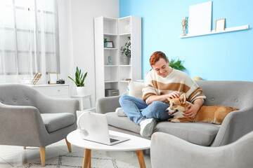 Redhead young happy man with cute Corgi dog sitting on sofa at home