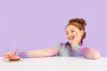 Obraz na płótnie Canvas Beautiful young happy woman with birthday cupcake on table against purple background