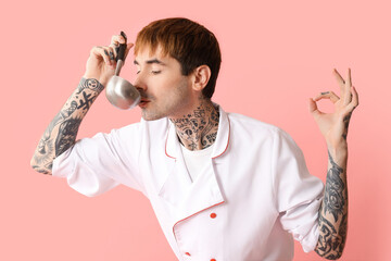 Tattooed male chef with ladle showing OK gesture on pink background
