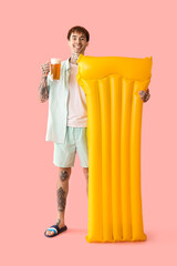 Obraz premium Tattooed young happy man with inflatable mattress and mug of beer on pink background