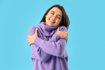 Beautiful young happy woman hugging herself on blue background - obrazy, fototapety, plakaty