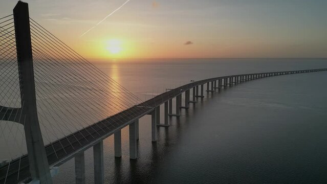 Drone flyover of Vasco da Gama bridge over Tagus river in Lisbon, Portugal at sunset on the hrozion