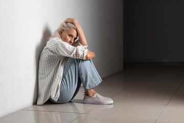 Depressed mature woman sitting near wall in dark hall