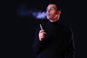 Fototapeta premium Young man smoking electronic cigarette on black background