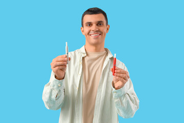 Young man with electronic cigarettes on blue background