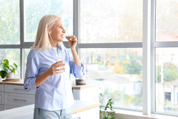 Mature woman with glass of water taking pills in kitchen