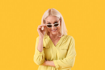 Mature woman with sunglasses on yellow background