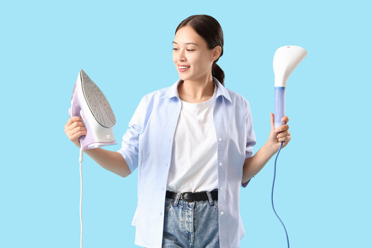 Young Asian woman with iron and garment steamer on blue background