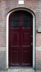 Fototapeta na wymiar Traditional Red Door with Arched Frame on Brick Building