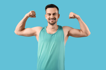 Fototapeta premium Handsome young man in sportswear showing muscles on blue background
