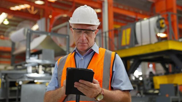 American older Engineer or worker wear hard Hat working in a factory with heavy machinery. Industrial Specialist Standing in Metal Construction Manufacturing technicians assistant workers in warehouse