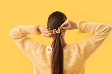 Beautiful young woman with silk scrunchy on ponytail against yellow background