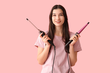 Beautiful young happy woman with curling irons on pink background