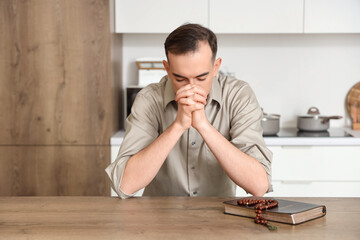 Young man praying at table in kitchen