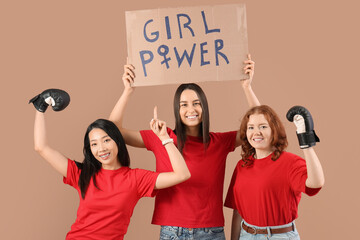 Beautiful young happy women in boxing gloves pointing at paper with text GIRL POWER on beige...
