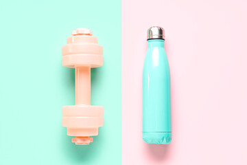 Dumbbell and bottle of water on color background
