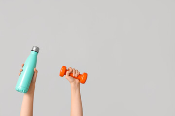 Female hands with bottle of water and dumbbell on grey background