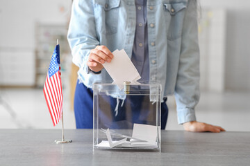 Voting young woman with USA flag near ballot box on table at polling station, closeup