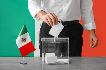 Voting young man with Mexican flag near ballot box on table at polling station, closeup