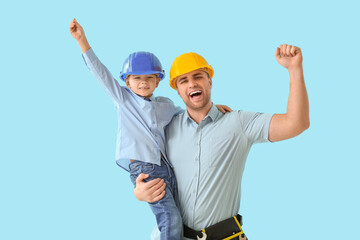 Happy father and his little son in hardhats with tools on blue background