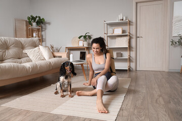 Sporty young African-American woman with yoga mat and cocker spaniel sitting on floor at home