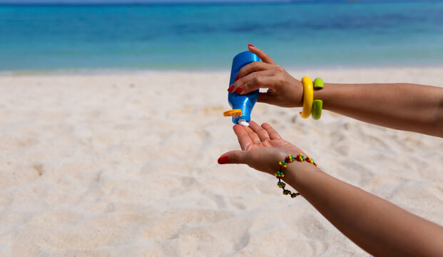 Woman hand with sunscreen cream on the sand beach as applying moisturizing lotion on .Skin care protection concept	