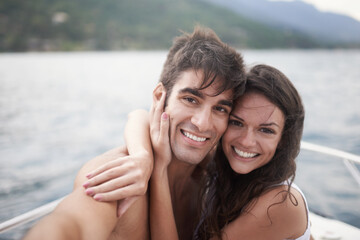 Fototapeta premium Portrait, selfie and happy couple at ocean on boat for vacation, holiday or travel together outdoor. Face, woman and man taking pictures at sea for adventure, hug and connection in summer on a ship