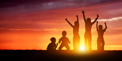 Children's happy silhouettes at sunset. Group of funny kids are jumping in the meadow on a summer...