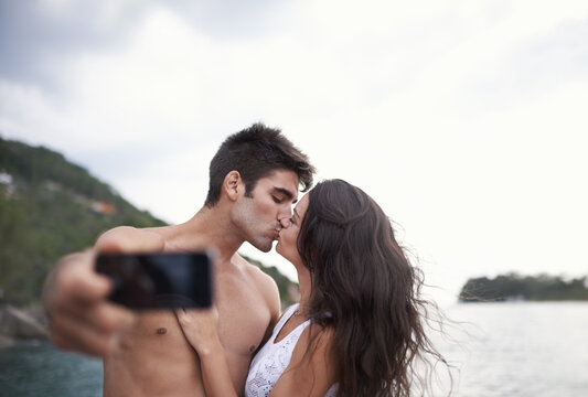 Kiss, selfie and couple at ocean for vacation, holiday or travel together outdoor. Photography, woman and man at sea for love, adventure and taking pictures for memory in summer by water in nature