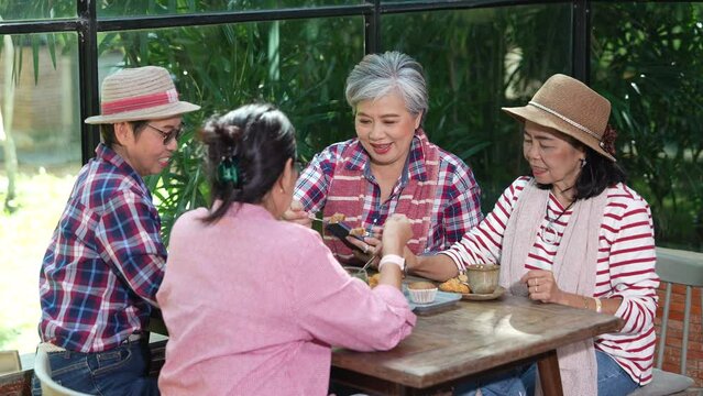 Group of Asian seniors, pensioners, elderly, and retirement friends laughing talking sharing health care spend free time get together at restaurant, happy using smartphone friendly technology learning