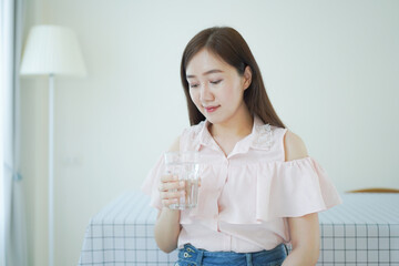 Cheerful Asian young woman drinking a water in a glass close up with copyspace. Asian working woman holding a glass of drinking water and smiling to camera. Work life balance concept.
