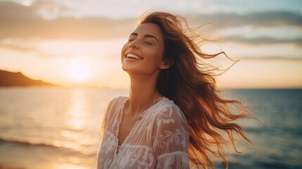A happy beautiful young smiling woman with hair flying in the wind, having fun on the beach with her eyes closed at sunset. Golden Hour, Pleasure, Joy, Travel, Summer, Vacation concepts.