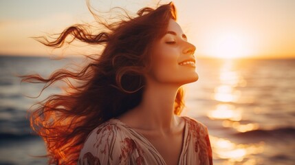 A happy beautiful young smiling ginger woman with long hair flying in the wind, stands on the seashore with her eyes closed at sunset. Golden Hour, Pleasure, Joy, Travel, Summer, Vacation concepts.