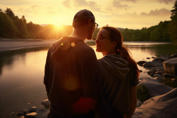 affectionate couple at a riverbank at sunset - obrazy, fototapety, plakaty