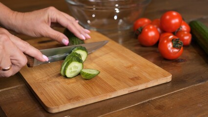 My kitchen is garden where woman slices cucumbers with knife preparing them for refreshing salad...