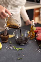 Woman pours soy sauce into glass bowl making marinade to marinate Pieces of Fresh tuna Fish fillet