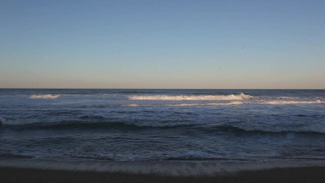 A scenic sunset view of waves breaking along the shore of a beach in Nags Head, Outer Banks, North Carolina.