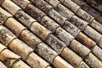 Old roof tiles on a house, aged and weathered and discolored. Texture and pattern of roofing made of terracotta, ceramic or clay.