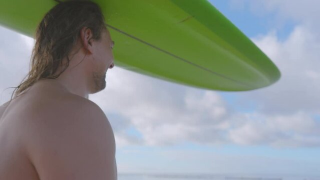 Close up barechested man effortlessly balances a green surfboard on his head, trying to find liquid leisure on both land and water.