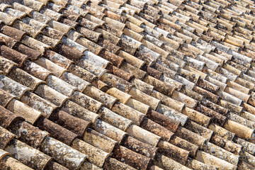 Old roof tiles on a house, aged and weathered and discolored. Texture and pattern of roofing made of terracotta, ceramic or clay.