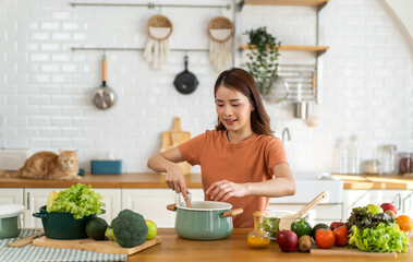 Young woman standing near stove and cooking, housewife, meal, chef, food.Happy woman looking and smelling tasting fresh delicious from soup in a pot with steam at white interior kitchen