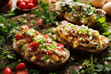 Sandwiches with scrambled eggs and various vegetables,  sprinkled with  fresh herbs on a wooden table, close up view