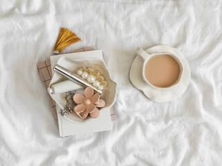 A cozy morning in bed - a cup of tea with milk, a bowl of cream, a hair clip, mascara, notebooks on...