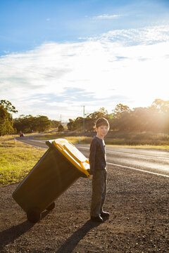 Young boy doing job taking bin across the road