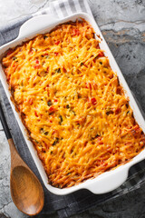 King Ranch Chicken Casserole combines juicy chicken, colorful peppers, tortillas in a bubbly creamy cheesy sauce close-up in a baking dish on a marble table. Vertical top view from above